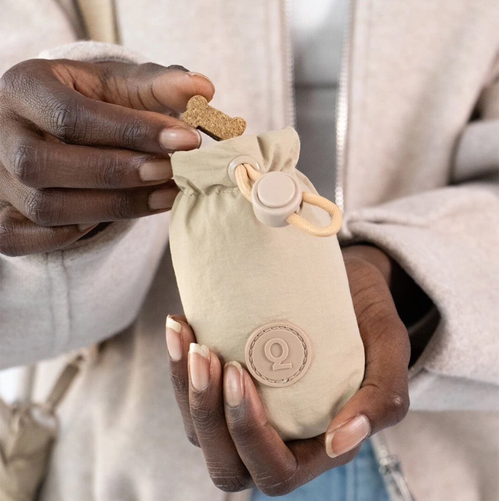 Mensch nimmt ein Leckerli aus dem Leckerlibeutel Treats Pouch in beige.