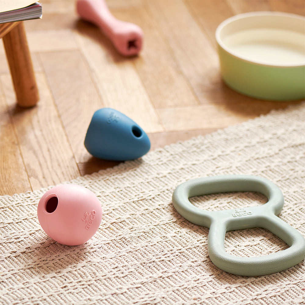 Verschiedene Spielzeuge von Beco aus Naturkautschuk liegen auf dem Boden einer Wohnung mit Holz-Parkett.