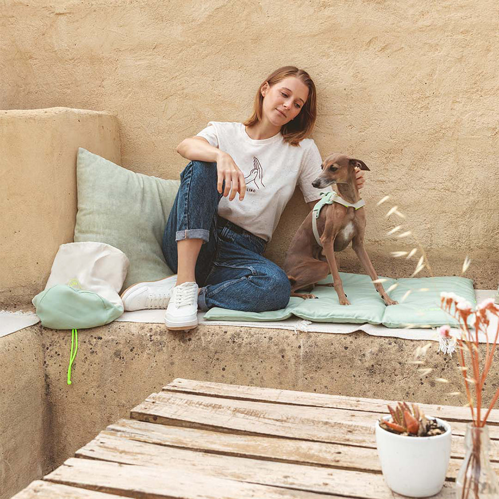 Mensch und Hund bei einer gemeinsamen Pause in der Natur. Hund sitzt auf der Hundematte in der Farbe: Mint.