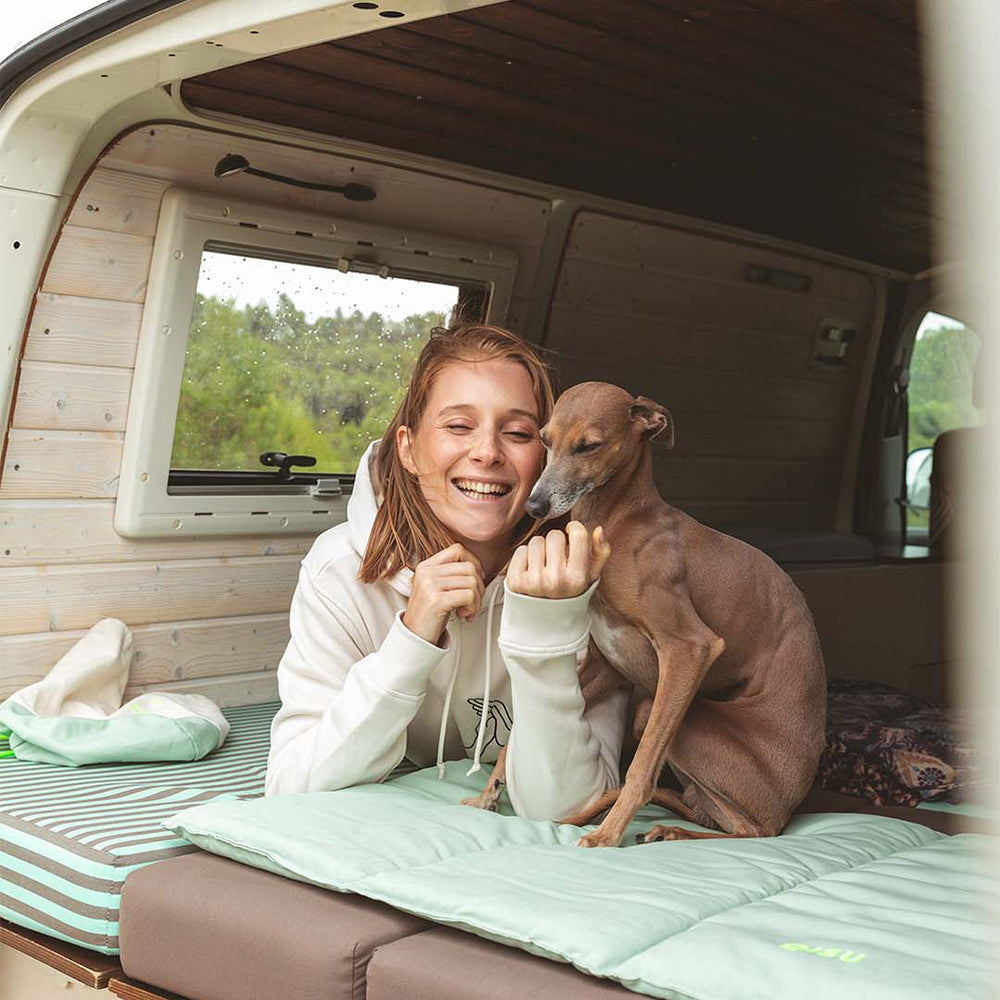 Hund und Mensch zusammen im Van. Hund sitzt auf der Hundematte von Qisu - Nomad Bed in der stilvollen Farbe: Mint.